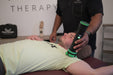Practitioner using a Rapid Release massager on a man lying on a treatment table