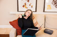 Woman using the Rapid Release Traveler on her neck while relaxing on a sofa with a carrying case beside her