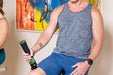 Man using a Rapid Release massager on his thigh beside a stationary bike